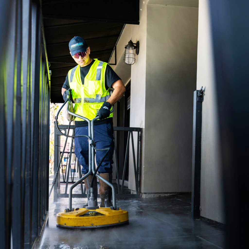 A man in a bright yellow vest is engaged in cleaning a floor, demonstrating attention to detail in his work